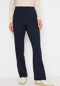 Navyblauwe flared broek van zachte stretchstof met een gladde tailleband en subtiele zijkanten stiksels, gecombineerd met lichte sneakers.