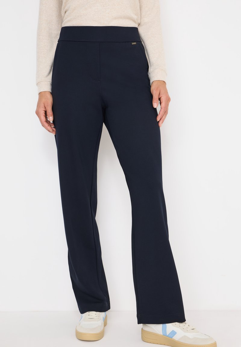 Navyblauwe flared broek van zachte stretchstof met een gladde tailleband en subtiele zijkanten stiksels, gecombineerd met lichte sneakers.
