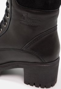 Bottine en cuir noir à surface texturée, avec œillets en métal, lacets ronds et talon en caoutchouc épais à bord dentelé.