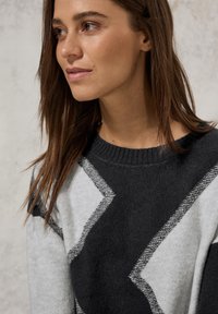 Pull en maille à motifs géométriques gris et noir avec un col rond et des poignets côtelés ; texture douce, avec des lignes en zigzag contrastantes.