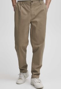 Chino w kolorze khaki wykonane z bawełny w luźnym kroju, z zapięciem na guzik i dwiema przednimi kieszeniami, w połączeniu z białymi sneakersami.