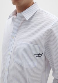 Camicia bianca con strisce verticali azzurro chiaro, taschino sinistro sul petto e dettaglio ricamato "Weekend Mood" sulla tasca.
