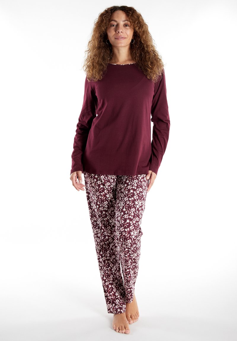 Maglia lunga color mogano con scollatura rotonda, abbinata a pantaloni bianchi con motivo floreale, realizzati in tessuto morbido e con una vestibilità comoda.
