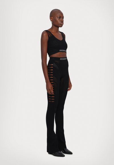 Must must crop top V-kaelusega ja suurte lõikeüksustega, koos kõrge vöökohaga, sügavalt istuvate leggingsidega, millel on horisontaalsed lõiked.