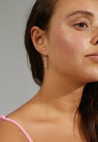 Boucles d'oreilles en argent avec trois maillons ronds, ornées de cristaux transparents. Texture lisse, design léger et crochets délicats pour un port sécurisé.