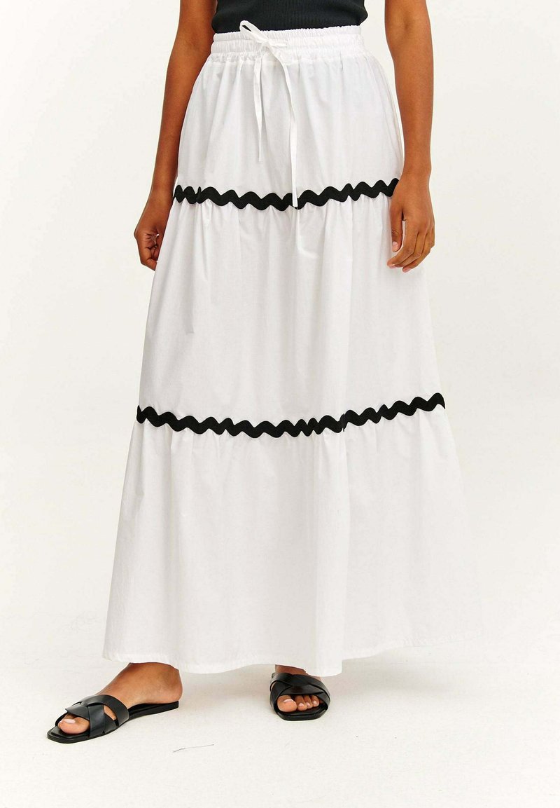 Weißer Maxirock mit schwarzer, gewellter Kante, ausgestattet mit einem elastischen Taillenbund und einem Kordelzug. Kombiniert mit schwarzen Slide-Sandalen.
