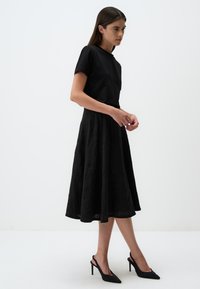 Top nero a maniche corte abbinato a una gonna nera ampia con tessuto testurizzato, indossato con scarpe con tacco a punta nere e a slingback.