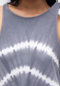 Débardeur gris en coton doux avec un motif tie-dye composé de cercles concentriques blancs et gris clair. Conception sans manches.