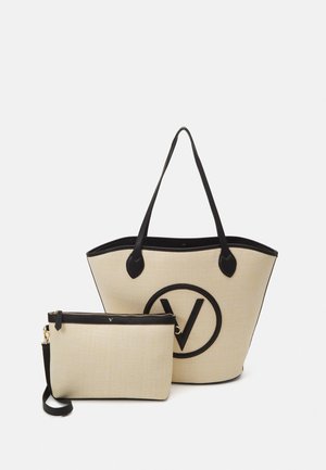 Bolsa de tote de tela beige con acentos de cuero negro, gran logotipo redondo y un pouch pequeño con cremallera a juego y correa para la muñeca. Textura suave.