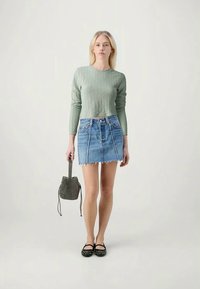 Light green ribbed long-sleeve sweater, denim mini skirt with frayed hem, black studded flats, and a patterned mini handbag.