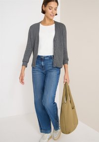 Cardigan grigio lavorato a maglia con chiusura a bottoni, t-shirt bianca, jeans blu e borsa tote leggera color oliva. Sneakers con un design beige e blu.