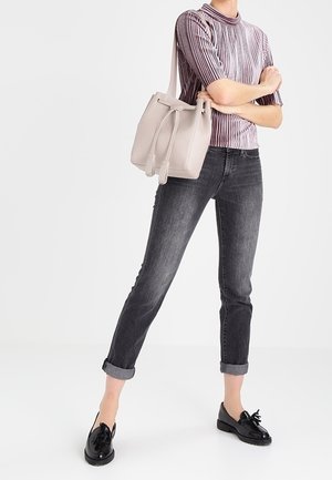 Jasnoszara torba na ramię z zaciąganym zamknięciem, koszulka w paski z krótkim rękawem, ciemnoszare spodnie z podwiniętymi nogawkami oraz czarne buty na sznurówki.