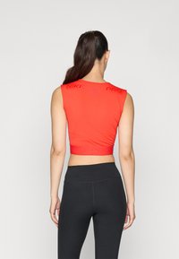 Rød, kort atletisk topp med korte ermer, med preget "NIKE PRO" merke, tettsittende design og glatt tekstur. Brukt med svarte tights.