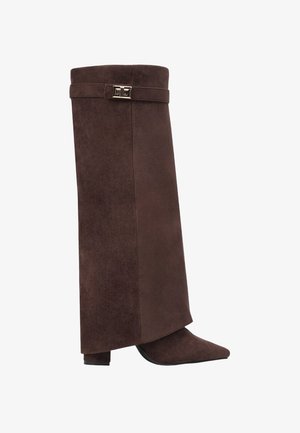 Botte en daim marron, haute, à bout pointu, avec un talon bloc et une sangle décorative avec une boucle métallique près du haut.