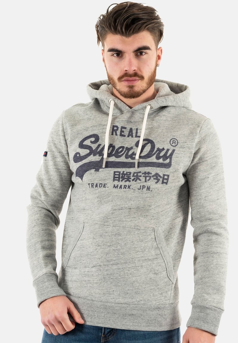 Felpa grigia con tasca a marsupio, cordini regolabili e logo "SuperDry" in blu scuro. Realizzata in un morbido tessuto testurizzato.