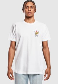 Hvid T-shirt med korte ærmer, der har et kyllingeemblem i en hexagonal ramme. Blødt bomuldsstof med en afslappet pasform og uformelt design.