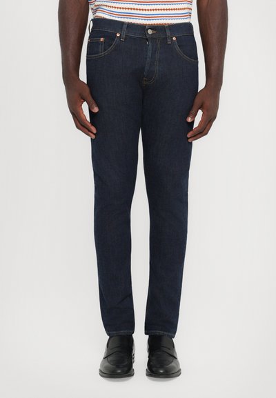 Dark blue denim jeans with a slim fit, featuring a classic five-pocket design and copper-colored hardware accents.