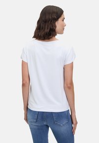 T-shirt blanc à manches courtes, avec un col rond, une texture lisse et une coupe décontractée, associé à un jean en denim bleu.