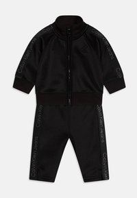 Tuta nera realizzata in tessuto morbido, composta da una giacca con zip e pantaloni affusolati. Caratterizzata dal logo "Calvin Klein Jeans" in grigio lungo i lati.