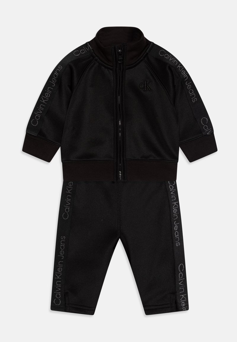 Tuta nera realizzata in tessuto morbido, composta da una giacca con zip e pantaloni affusolati. Caratterizzata dal logo "Calvin Klein Jeans" in grigio lungo i lati.