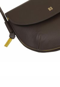 Borsa a spalla in pelle marrone con pattina curva, interno giallo, dettagli gialli e branding dorato minimalista. Superficie testurizzata con dettagli di cucitura.
