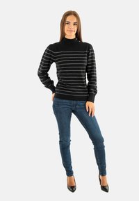 Zwart gestreepte trui met een hoge kraag, geribde manchetten en zoom. Gedragen met blauwe slim-fit jeans en zwarte hakken. Glad textuur en aansluitend ontwerp.