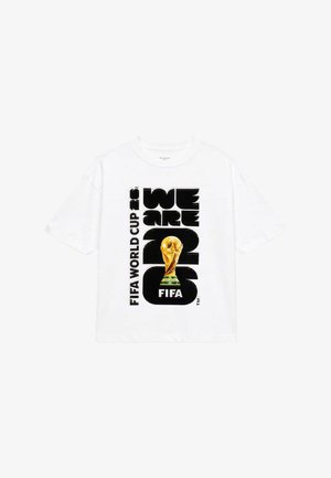 Hvid T-shirt med sort tekst "WE ARE 2026" og "FIFA WORLD CUP 26" sammen med et stort billede af FIFA World Cup-trofæet i guld.
