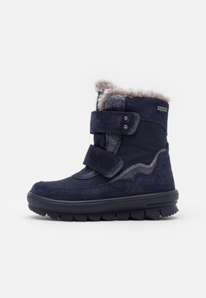 Bota de invierno azul marino con dos cintas de velcro, forro de piel en la parte superior, suela gruesa con dibujo y etiqueta impermeable Gore-Tex.