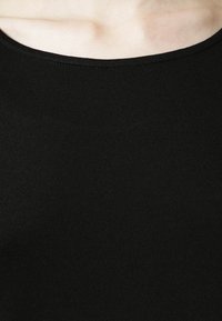 Tissu en tricot noir avec une texture douce ; présente un col rond et une coupe extensible, adapté à différents types de corps et aux superpositions.