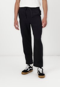 Czarne spodnie z teksturowanej tkaniny z elastyczną talią i sznurkiem, zestawione z czarno-białymi trampkami na gumowej podeszwie.