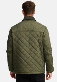 Grøn quiltet jakke med diamantskærmsmønster, der har krave og ribbede manchetter. Materialet ser polstret ud for varme og komfort.