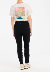 Kremowa koszulka z kolorowym nadrukiem krajobrazu; dopasowane czarne spodnie; beżowe sportowe buty; gładki materiał, casualowy design i slim fit.