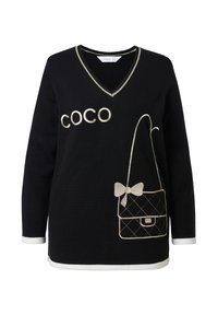 Suéter negro con cuello en V, ribete blanco y un gran texto "COCO". Diseño de bolso bordado con un lazo y un patrón acolchado.