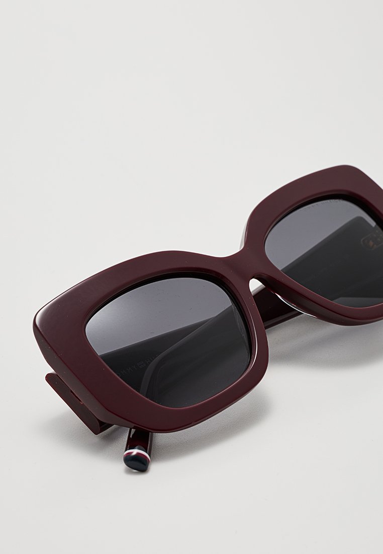 Occhiali da sole oversize bordeaux con lenti scure, montatura quadrata spessa e finitura lucida; presenta un accento multicolore sul braccio.