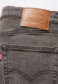 Jeans Levi's gris foncé avec poche arrière et patch en cuir beige portant la taille W32 L32 et le logo.