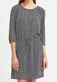 Schwarz-weiß gemustertes Kleid mit Rundhalsausschnitt, Dreiviertelärmeln und elastischem Bund für eine lockere Passform. Glatte Stofftextur.