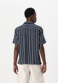 Chemise à manches courtes bleu marine avec des rayures verticales blanches, en tissu léger, coupe décontractée, avec un col pointu et un ourlet droit.