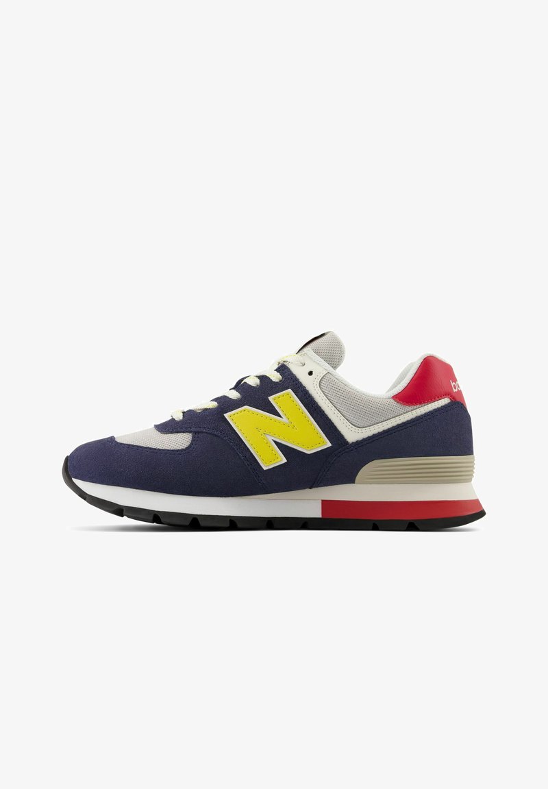 Chaussure de sport bleu marine et grise avec un logo "N" jaune, un accent rouge au talon, une semelle blanche, en daim et maille, avec des coutures contrastées.