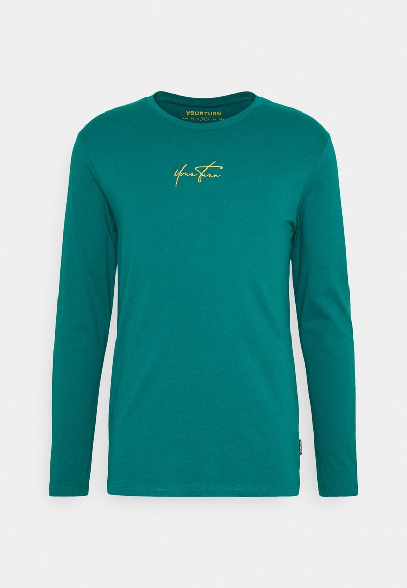 Long-sleeve teal t-shirt made of soft cotton. Features a round neckline and a gold cursive logo on the chest. Smooth texture, casual fit.