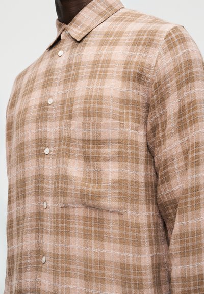Άνδρας που φοράει πουκάμισο με ταμπλόγια σε μπεζ και ανοιχτό καφέ χρώμα με τσεπάκι στο στήθος, εμφανιζόμενος από τους ώμους μέχρι τη μέση του κορμού.