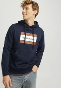 Hoodie marine en mélange de coton doux, doté d'une poche kangourou à l'avant et d'un grand graphique logo en blanc et rouille sur la poitrine.