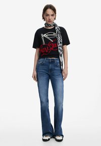 Must musta, millel on punane kirsi graafika, sinised laiad teksad ja must-valge triibuline sall; vabalt voolav lõige, pehme kangas ja klassikaline denim tekstuur.
