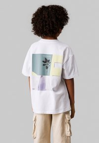 Camiseta de algodón blanca con un gráfico en la parte posterior que presenta una palmera, formas abstractas en azul y amarillo, y el texto "Calvin Klein Jeans".