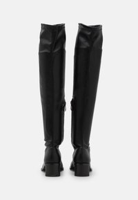 Botas de cuero negras por encima de la rodilla con un diseño elegante, que cuentan con una superficie texturizada y un robusto tacón cuadrado. Cremalleras laterales para el cierre.