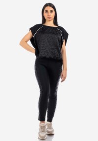 Top nero a maniche corte con motivo testurizzato e piping bianco, abbinato a leggings neri con un motivo sottile, indossato con sneakers beige.