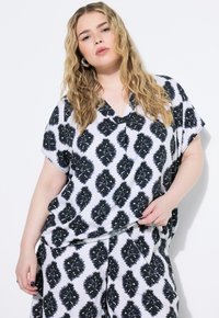 Maglietta a maniche corte, dalla vestibilità ampia, di colore bianco con un motivo astratto nero. Presenta un design a scollo a V e un tessuto morbido e texturizzato.