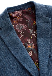 Blazer bleu foncé à motif pied-de-poule avec une riche doublure florale bordeaux, présentant une texture lisse et des revers structurés.