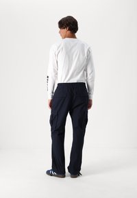 Marina cargo byxor med två stora sidofickor, elastisk midja och bakfickor, i kombination med en långärmad vit T-shirt.
