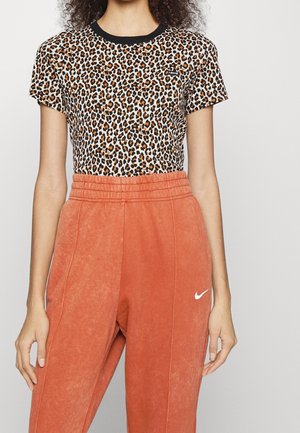 Kobieta ubrana w krótki top w panterkę z czarnym kołnierzykiem i pomarańczowe spodnie dresowe z wysokim stanem, z białym logo Nike.