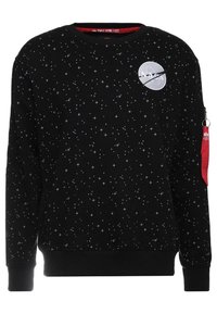 Svart sweatshirt med vit stjärnmönster, NASA-logotyp på bröstet, röd textilflik fäst vid dragkedjan på vänster ärm.